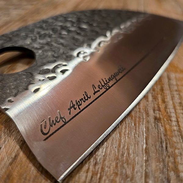 Close-up of a chef's knife blade with engraved name on a wooden surface
