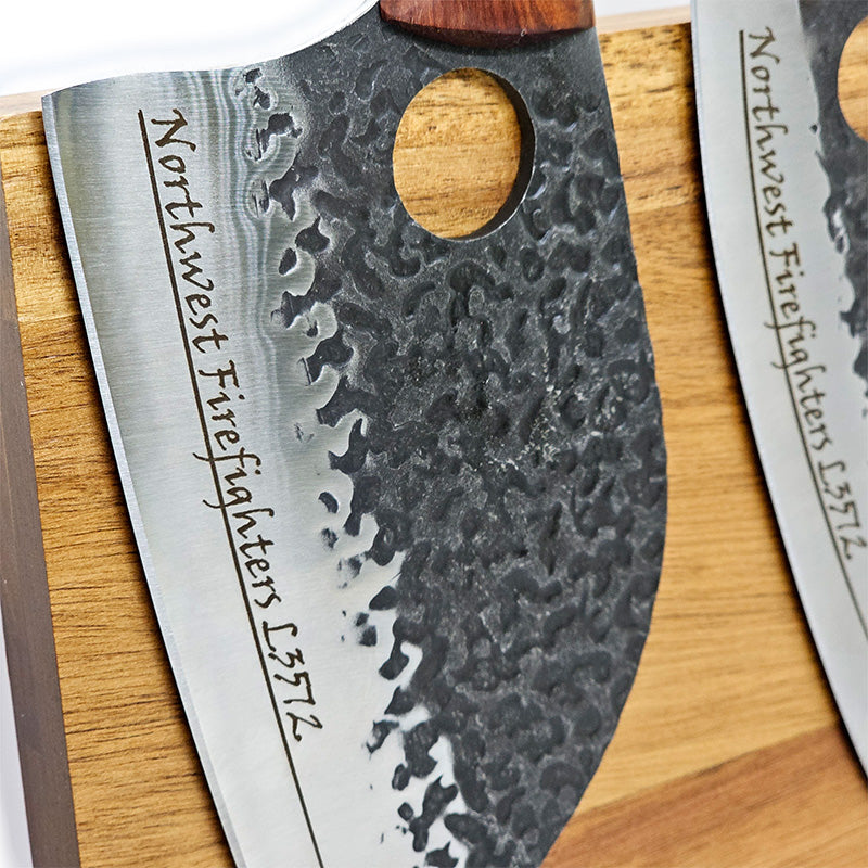 Hammered steel butcher knife with textured blade and wooden handle on a wooden surface, featuring 'Northwest Firefighters L3572' engraving.