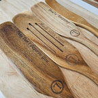 Wooden utensils with engraved text on a light wooden surface
